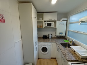 Een kleine keuken met een wasmachine, magnetron en raam met uitzicht.