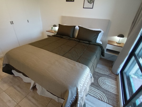 Een slaapkamer met een groot bed, nachtkastje, lamp en raam.
