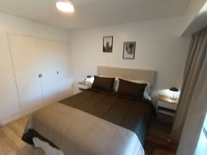 Un dormitorio con una cama grande, mesitas de noche, un armario y dos cuadros en la pared.