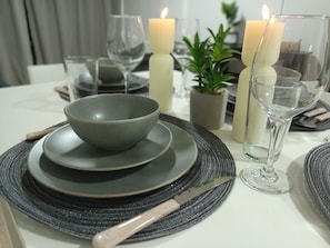 Una mesa servida con platos, tazones, cubiertos, vasos y velas.