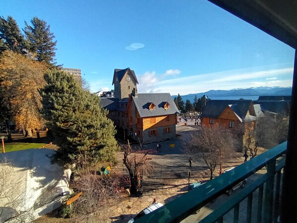 Vista de un pueblo con una destacada torre del reloj, un edificio de piedra y una masa de agua en la distancia.