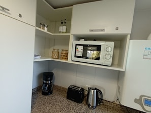 Een kitchenette met een magnetron, broodrooster, koffiezetapparaat en waterkoker.