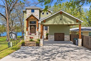 A two-story house with a stone facade, a front porch with a wooden railing, and a garage with a wooden door. - The Lakeside Blessing on Lake Dunlap (New Braunfels)