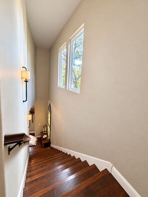 A hallway with wooden flooring, a staircase, and a window with a view of trees. - The Lakeside Blessing on Lake Dunlap (New Braunfels)