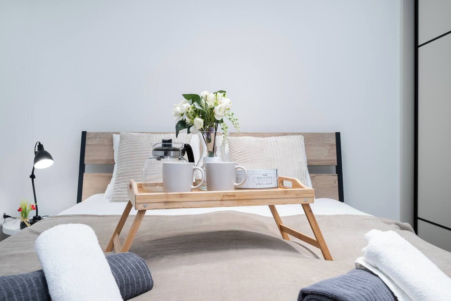 Een net opgemaakt bed met een dienblad waarop een koffiepot, twee mokken en een doos koekjes staan.