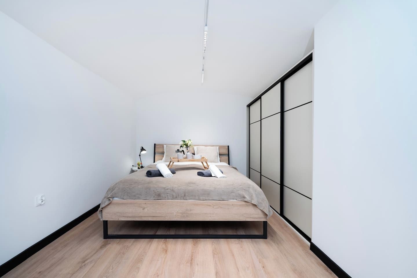 Ein modernes Schlafzimmer mit minimalistischem Design, ausgestattet mit einem Bett mit Holzrahmen, einem Nachttisch mit Lampe und einem großen Fenster.