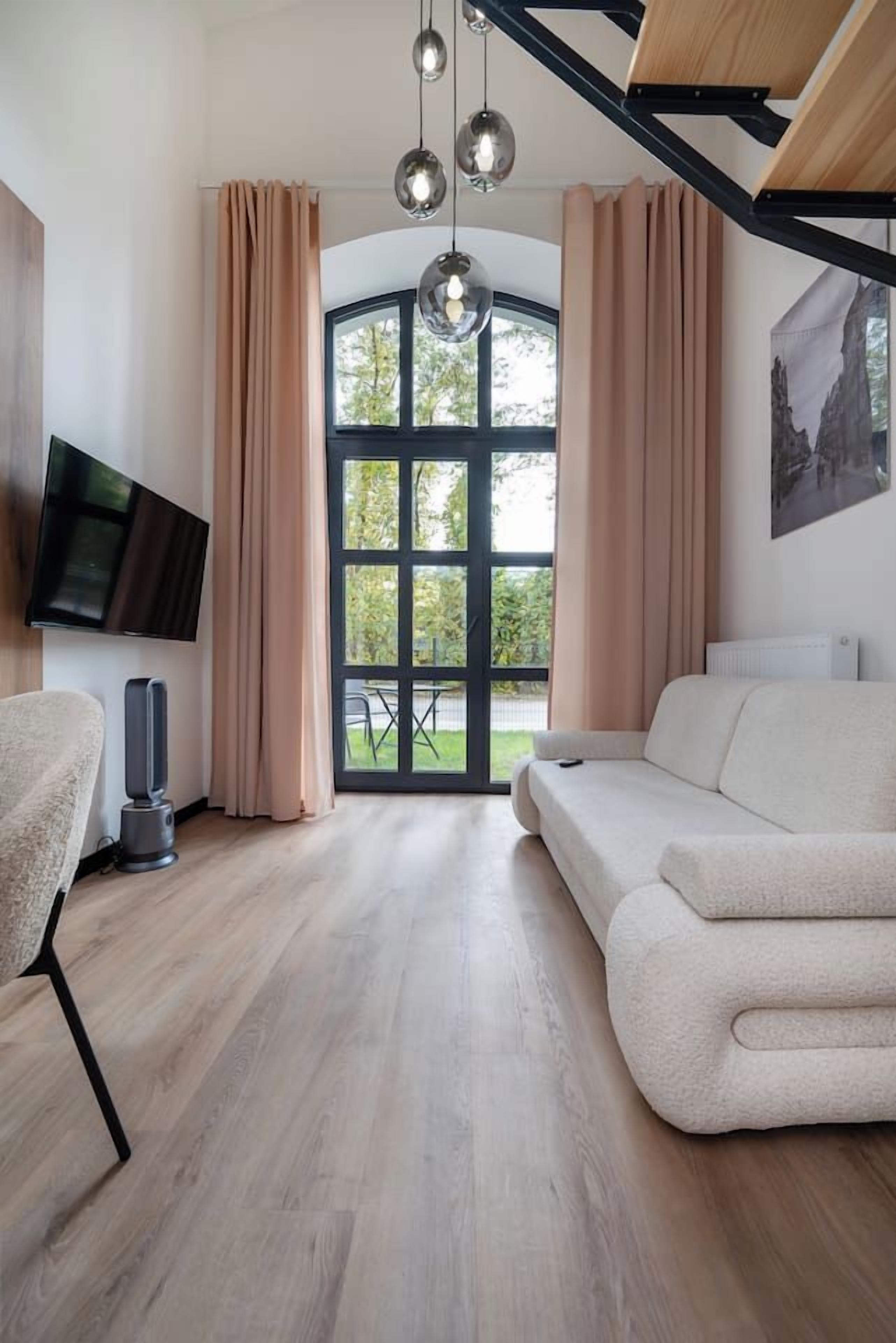 Een moderne woonkamer met een bank, een televisie en een groot raam met gordijnen.
