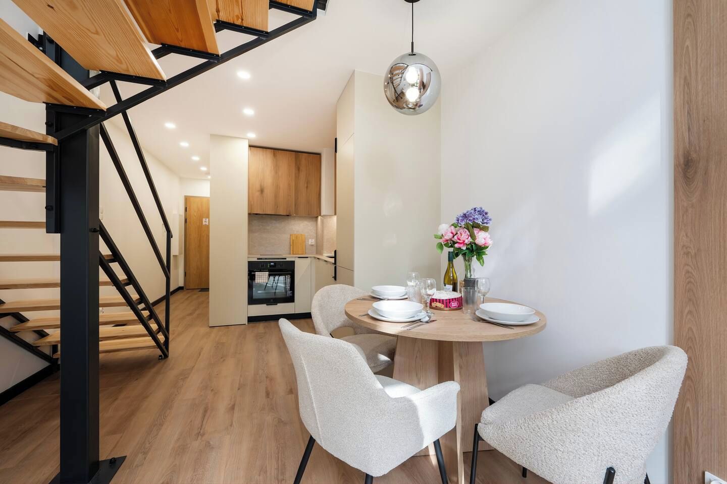 Een moderne keuken met houten kastjes, een inbouwoven en een eethoek met een ronde tafel en stoelen.