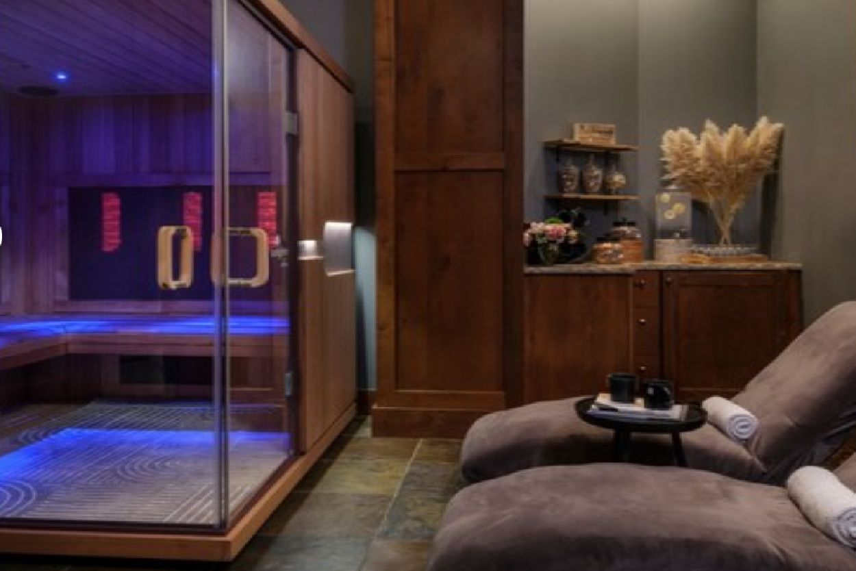 A room with a massage chair, a glass-enclosed sauna, and a wooden cabinet with decorative items.