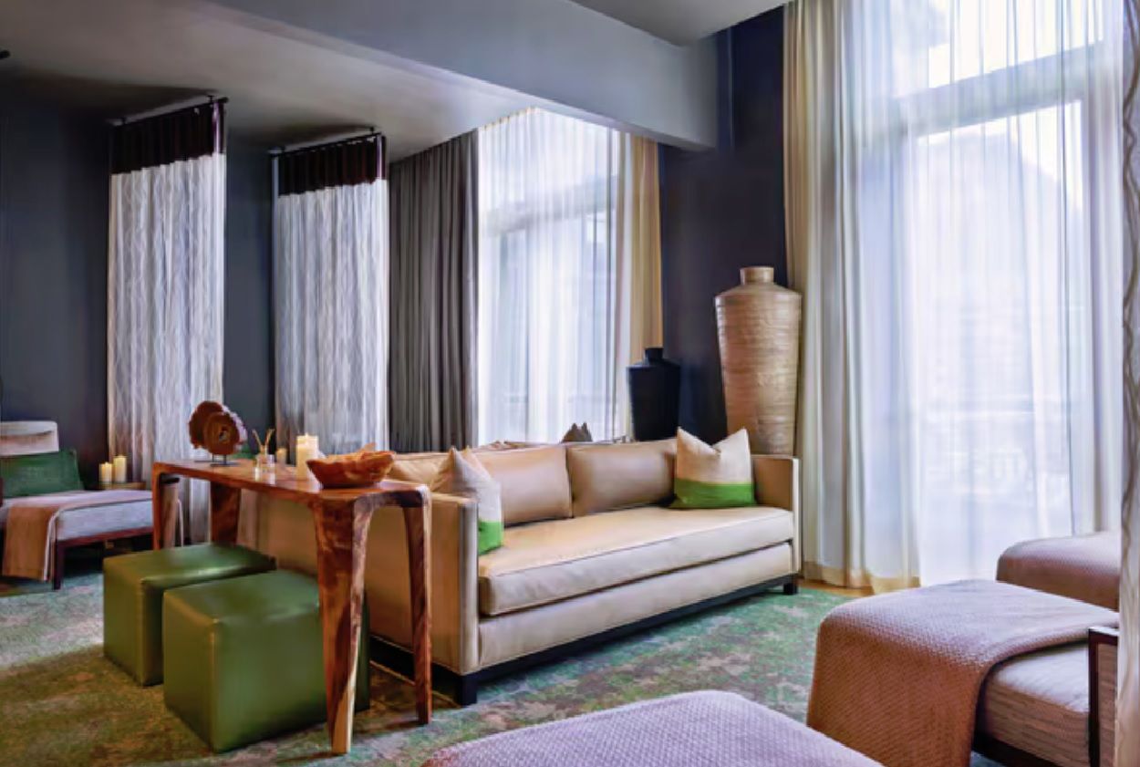 Una habitación de hotel con sofá, otomanas, una mesita de madera y un jarrón grande.