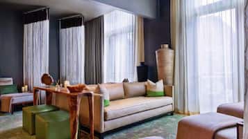 Una habitación de hotel con sofá, otomanas, una mesita de madera y un jarrón grande.