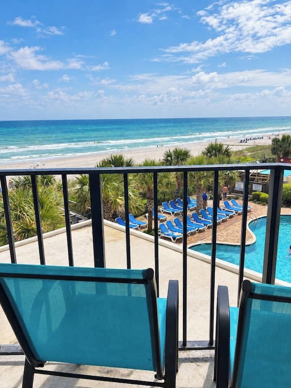 A balcony with blue chairs overlooking a pool and beach. - Coastal Cutie – Oceanfront Getaway. (Myrtle Beach)