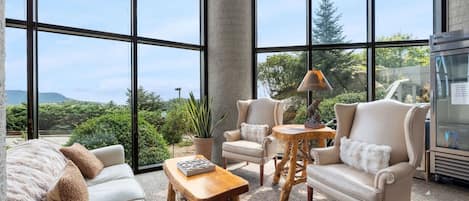 A spacious room with large windows, a sofa, two armchairs, a wooden coffee table, and a small table with a lamp.