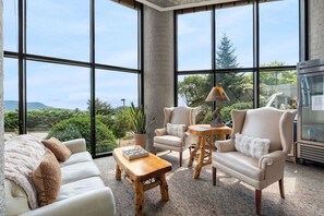 A spacious room with large windows, a sofa, two armchairs, a wooden coffee table, and a small table with a lamp. - 2BR High Floor Suite | Pool/Sauna | Mountain Views (Sugar Mountain)