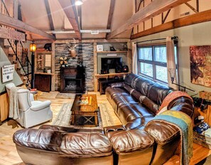 A cozy living room with a fireplace, leather sofas, a coffee table, and a television. - Hillside Haven- a cozy Getaway in the heart of Hocking Hills (Rockbridge- Hocking Hills (Hillside Haven))