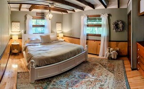 Ein Schlafzimmer mit einem großen Bett, Holzboden, einem dekorativen Teppich, einem Schminktisch und einem Fenster mit Vorhängen.