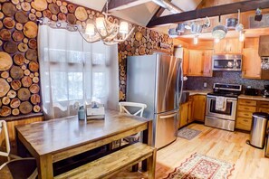 A kitchen with a central island, wooden cabinets, stainless steel appliances, and a chandelier. - Hillside Haven- a cozy Getaway in the heart of Hocking Hills (Rockbridge- Hocking Hills (Hillside Haven))