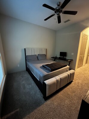 Une chambre à coucher avec un lit, un ventilateur de plafond, une table de chevet et une porte.