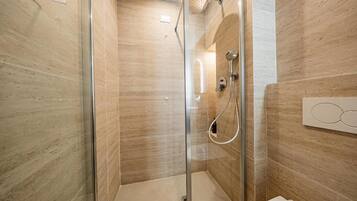Ein modernes Badezimmer mit einer gläsernen Duschkabine, einem weißen Waschbecken und einer wandmontierten Leuchte.