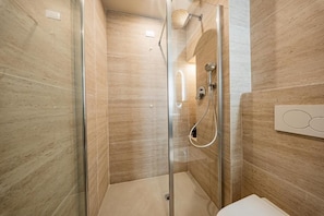 A modern bathroom with a glass-enclosed shower, a white sink, and a wall-mounted light fixture. - Lumi stays (Firenze)