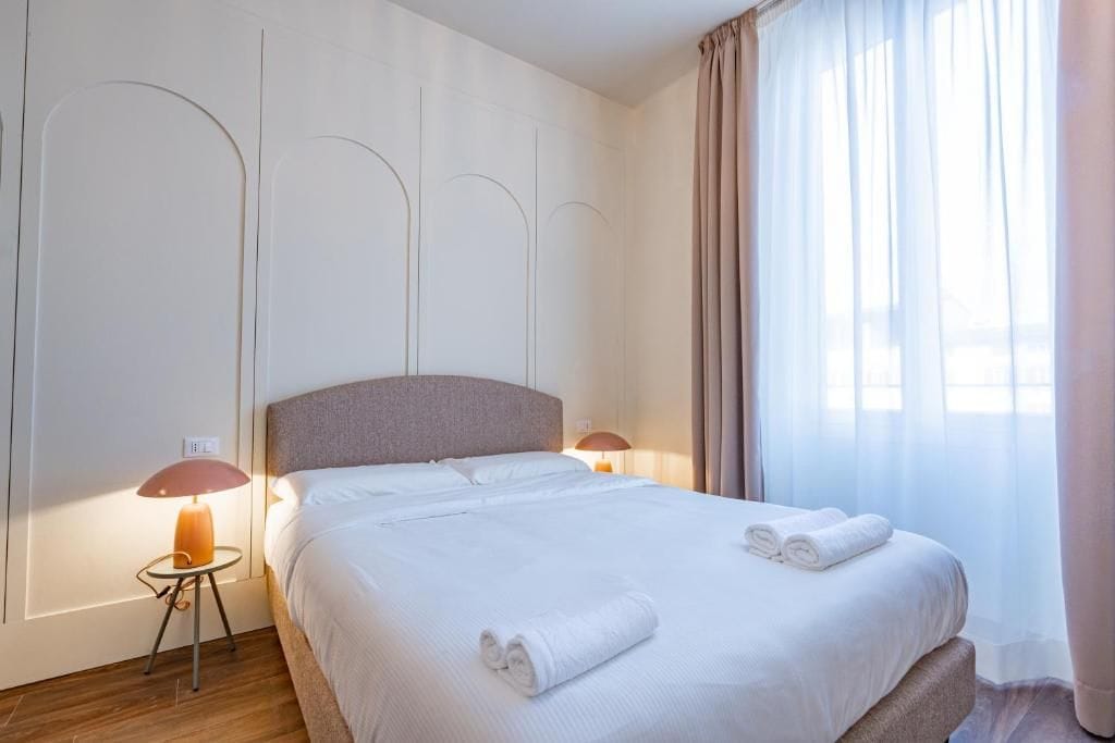 Ein Hotelzimmer mit einem großen Bett, zwei Nachttischlampen, einem fensterbelaubten Fenster und einer Wand mit einem einzigartigen Design.