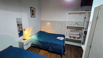 Un dormitorio con cama, mesita de noche con lámpara, armario y una pequeña estantería con una planta.