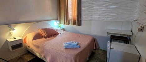 Ein Schlafzimmer mit einem Bett, einem Nachttisch, einer Lampe, Vorhängen und einem Wandheizkörper.
