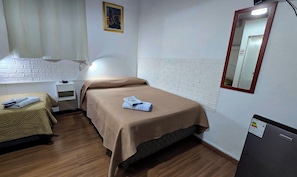 Habitación de hotel con dos camas, una mesita de noche, una lámpara, un espejo y un refrigerador.