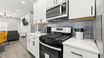 A modern kitchen with white cabinetry, a black stove, a microwave, and a tiled backsplash.