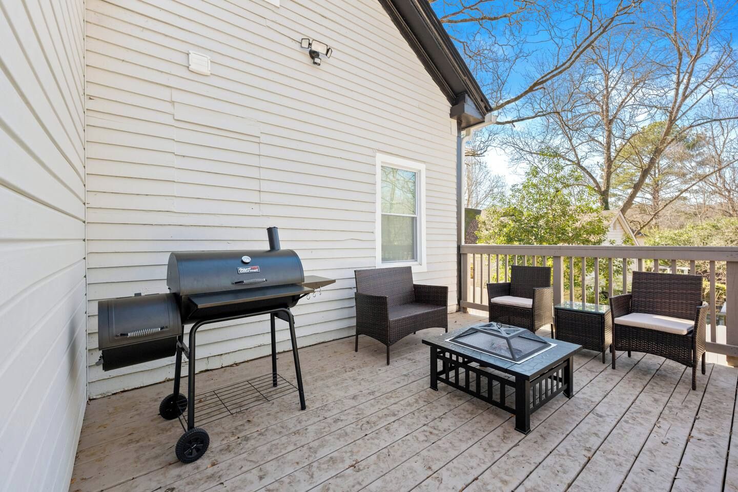 A covered outdoor deck with a barbecue grill, wicker furniture, and a glass table.