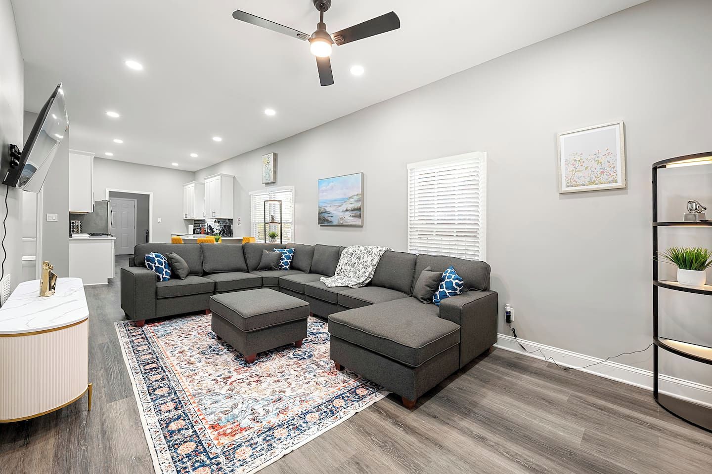 A modern living room with a sectional sofa, ottomans, a patterned rug, and a ceiling fan.