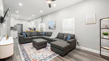 A modern living room with a sectional sofa, ottomans, a patterned rug, and a ceiling fan.