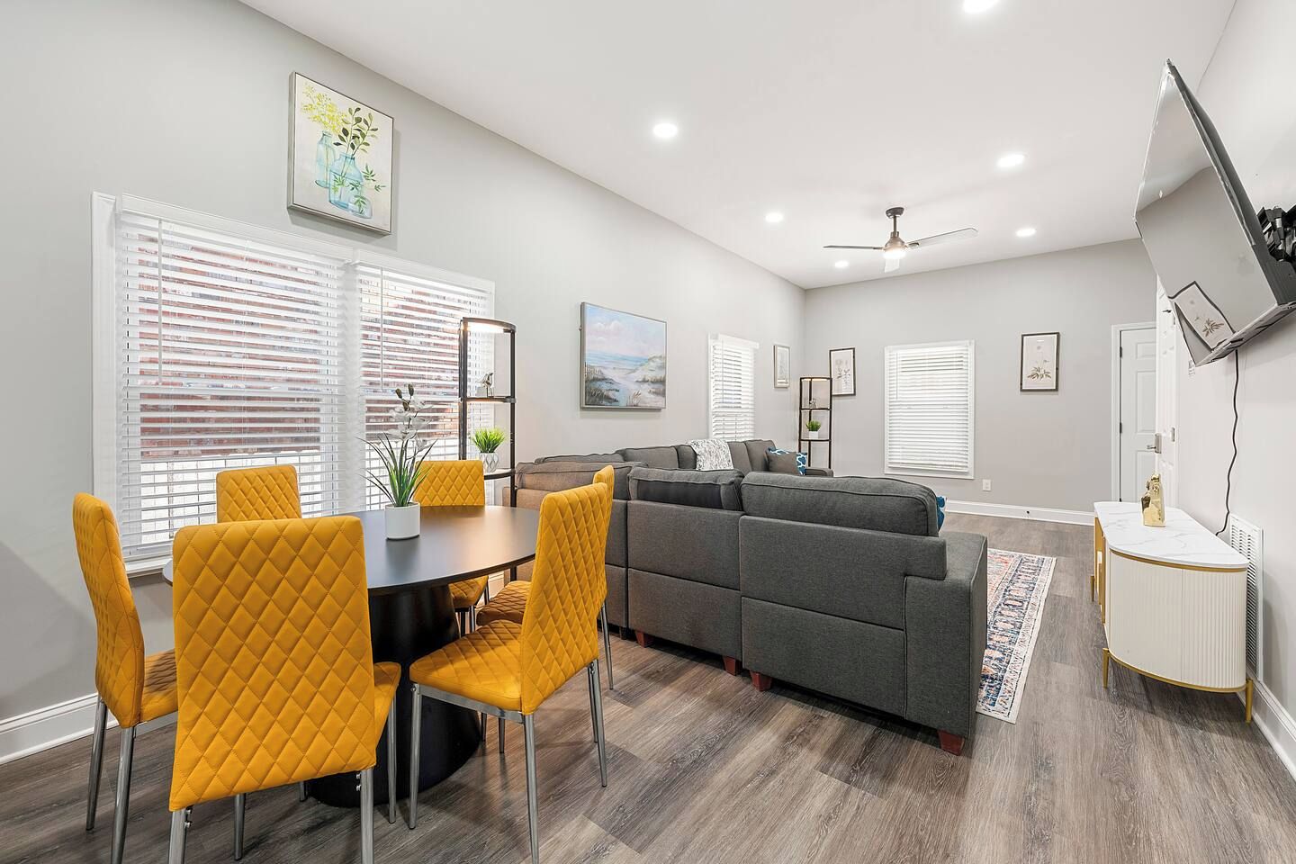 A modern living room with a grey sofa, yellow chairs, and a dining table with a white tablecloth.