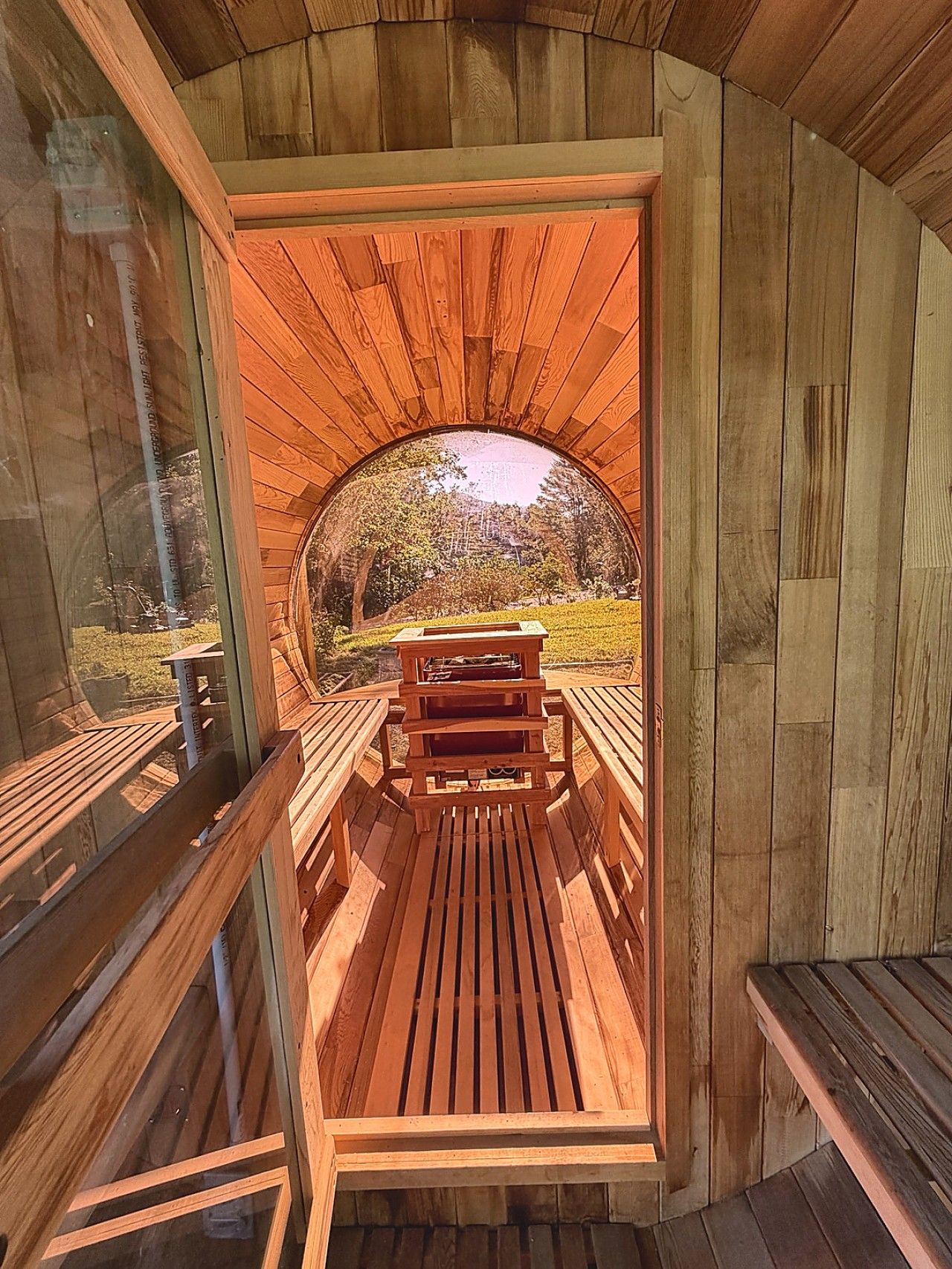A wooden structure with a bench and a table, a clear view of the outdoors, and a wooden floor.