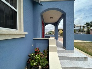 A blue building with a covered entrance, potted plants, and a view of neighboring houses. - ShaDow Villa - 3 Bedroom House Near Airport (Charnocks)