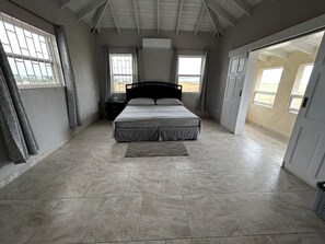 A bedroom with a bed, curtains, a nightstand, and a view through a window. - ShaDow Villa - 3 Bedroom House Near Airport (Charnocks)