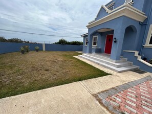 Ein Wohnhaus mit blauer Fassade, einer roten Tür und einem Vorgarten mit Rasen und Blumentöpfen.