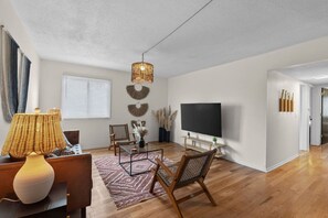 A modern living room with a flat-screen TV, a lamp, a chair, and a coffee table. - Designer Mid-Term Living Near Omaha Hospitals (Omaha)