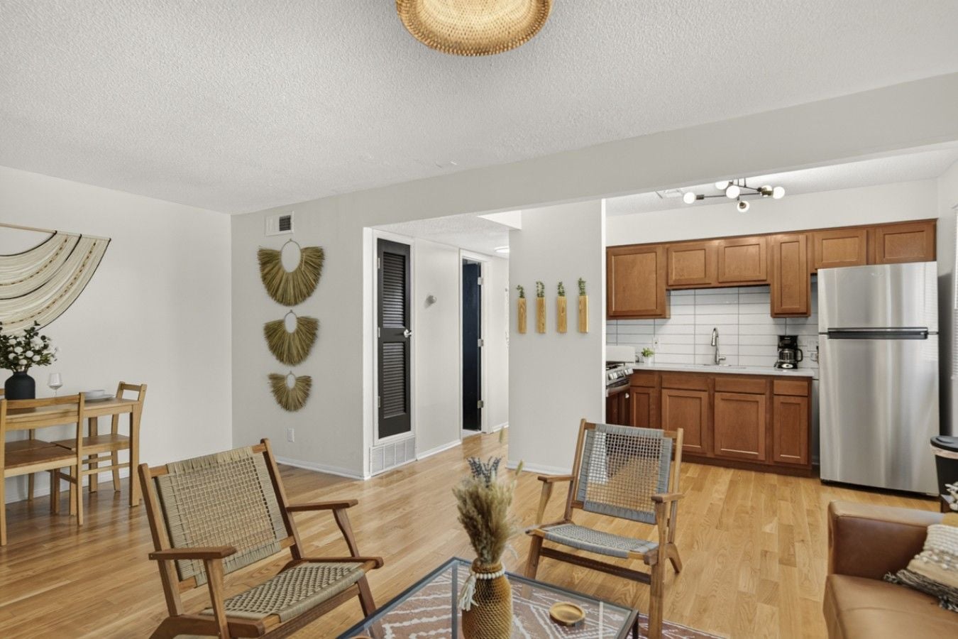 A modern kitchen with wooden cabinets, a stainless steel refrigerator, and a dining area with a table and chairs.