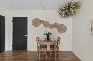 A dining area with a wooden table and chairs, a black door, and wall-mounted decorative items. - Designer Mid-Term Living Near Omaha Hospitals (Omaha)