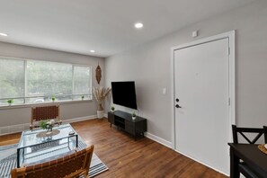 A modern living room with a glass coffee table, wooden chairs, a flat-screen TV on a black stand, and a white door. - Prime Location Midtown Omaha (Omaha)
