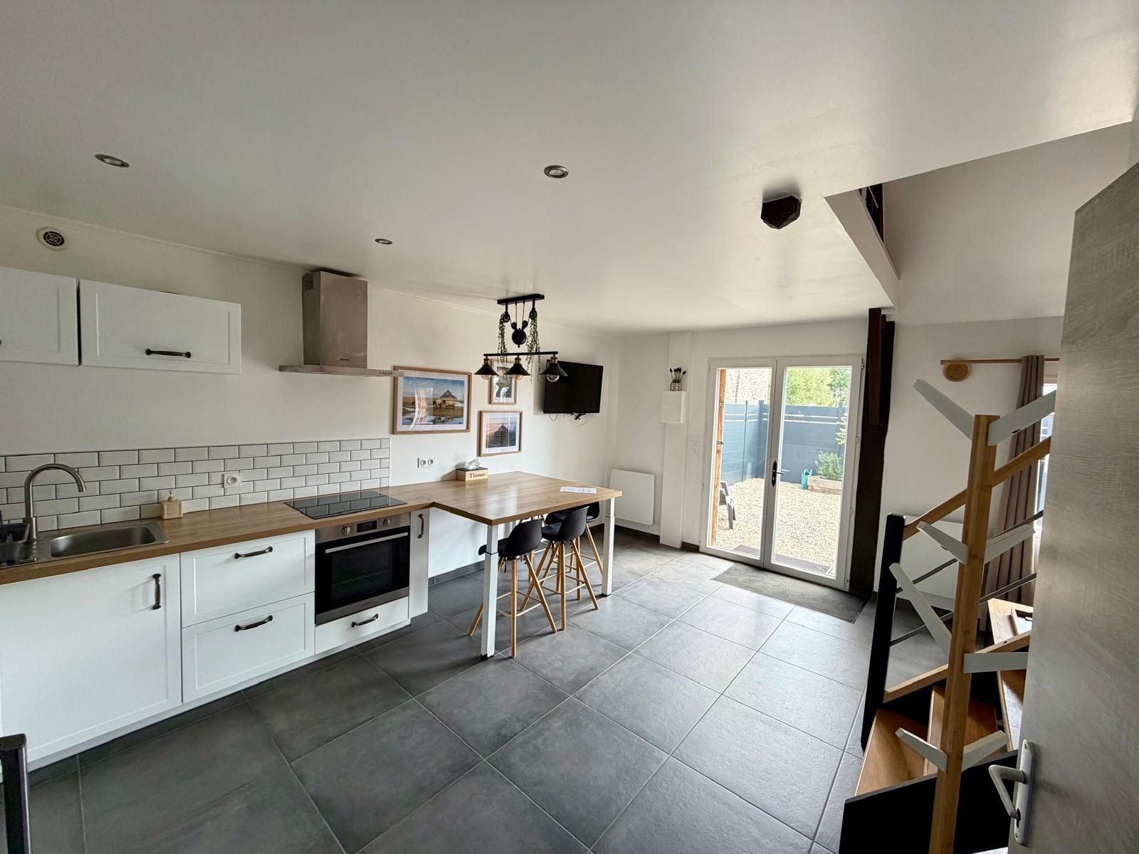 A modern kitchen with white cabinets, a wooden countertop, and a built-in oven. There is a dining area with a table and chairs, and a view of the backyard through a glass door.