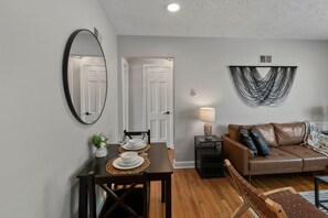 A dining area with a table set for two, a sofa, and a wall-mounted mirror. - Prime Location Midtown Omaha (Omaha)