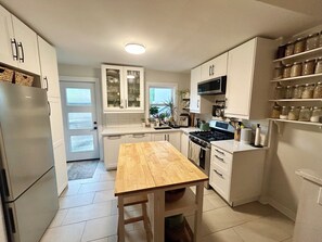 A kitchen with white cabinets, a wooden table, a stove, and a refrigerator. - Sweet Beach House in the City! Great neighbourhood; family and pet friendly (Toronto)