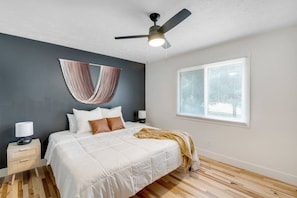 A bedroom with a bed, a ceiling fan, a window with blinds, a bedside table with a lamp, and a wall-mounted hammock. - Prime Location! HGTV Design! (Omaha)