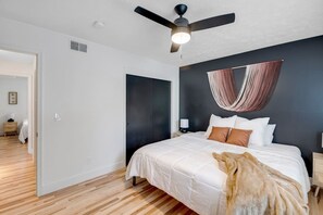 A bedroom with a bed, a ceiling fan, a hanging chair, and a wooden floor. - Prime Location! HGTV Design! (Omaha)