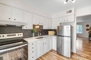 A modern kitchen with white cabinetry, a stainless steel refrigerator, and a built-in oven. - Prime Location! HGTV Design! (Omaha)