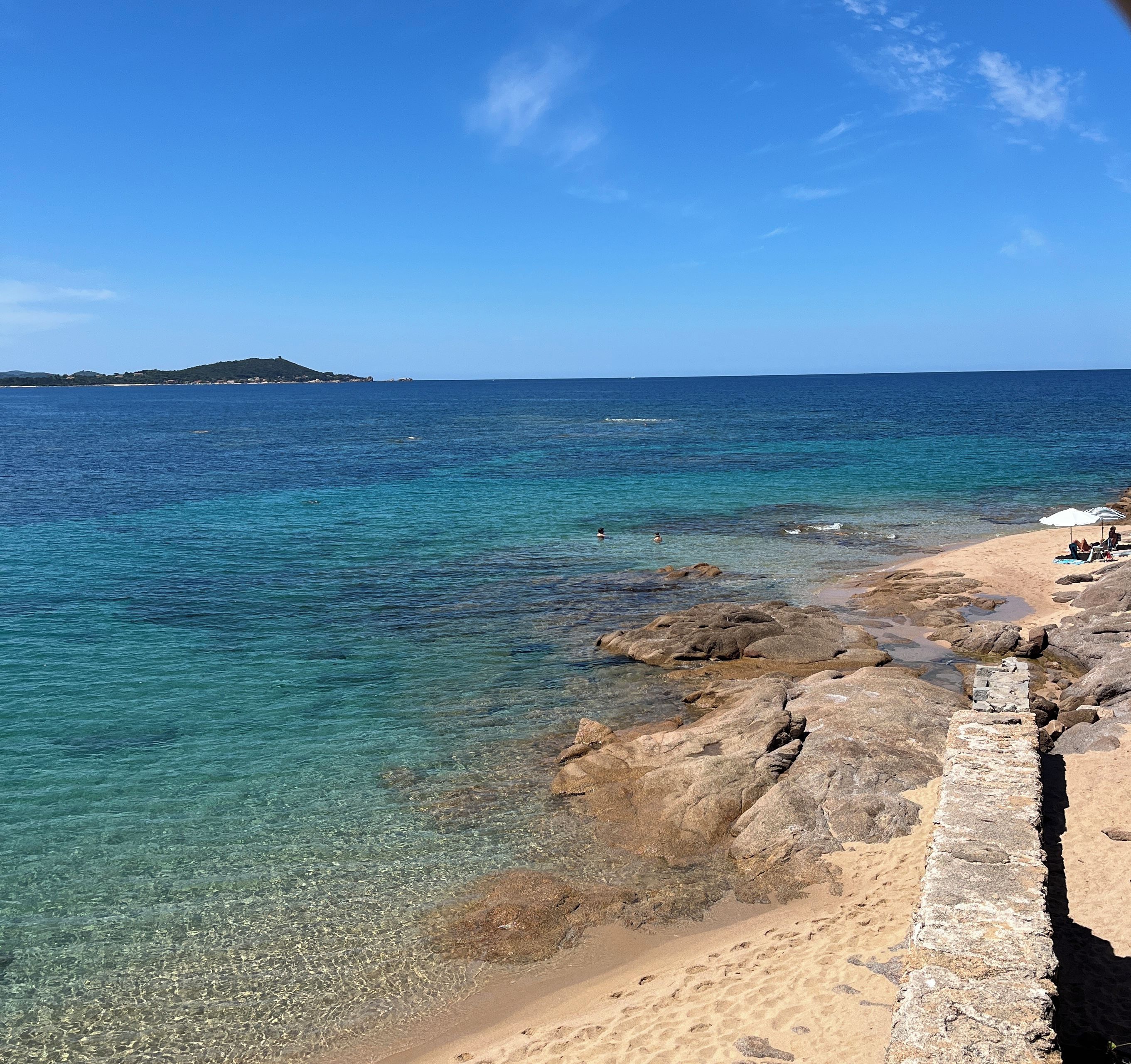 A coastal beach with clear water, rocky shoreline, and a distant island.