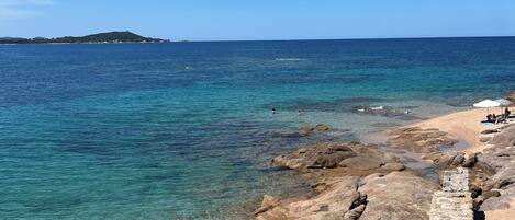 A coastal beach with clear water, rocky shoreline, and a distant island.