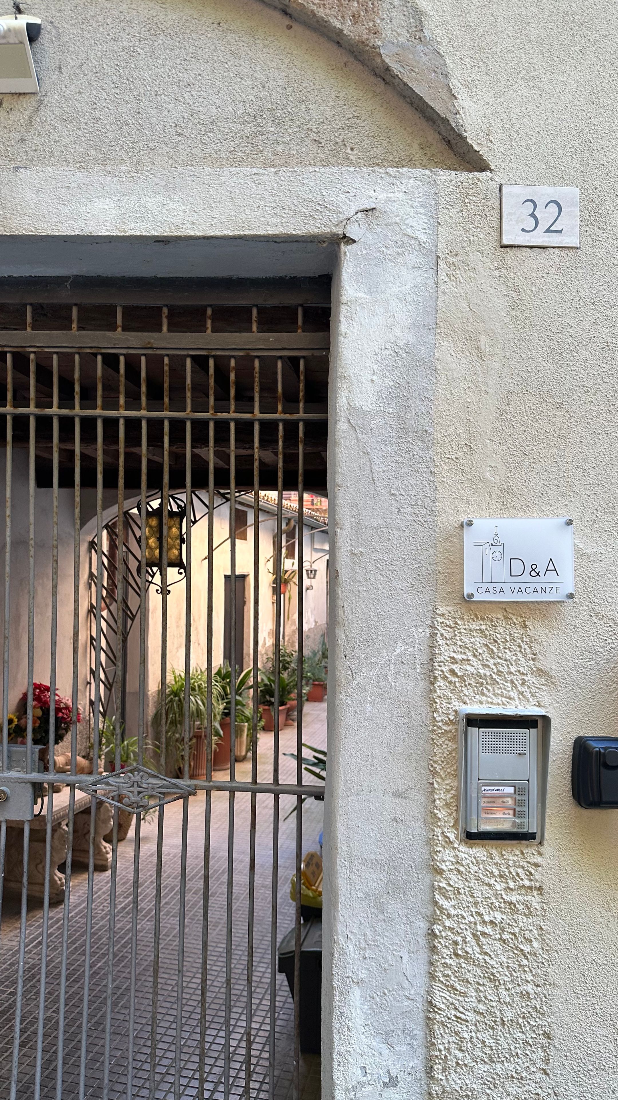 Una entrada vigilada con un letrero de número, un cartel de villa y un intercomunicador de seguridad.